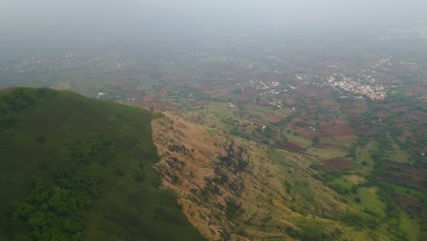 a drone captures the lush green mountains of panchgani, maharashtra, draped in monsoon mist. the vibrant landscape fades into soft clouds, with glimpses of the city nestled below in serene beauty