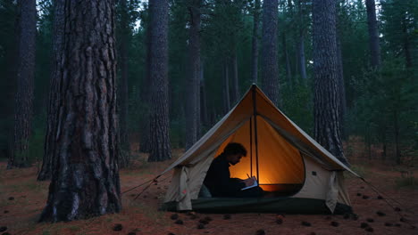 man camping and reading in a tent at night in the forest