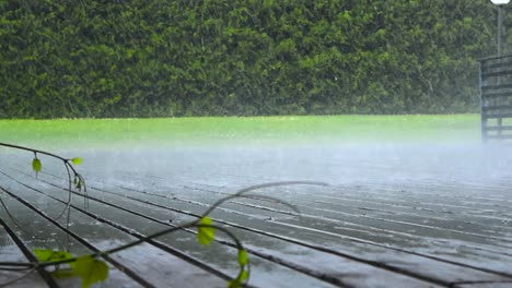 low angle video of heavy rainfall and hale falling on a wooden deck or a terrace during a summer or autumn day with ice pieces visible bouncing and green cut and mowed lawn grass in the wet background