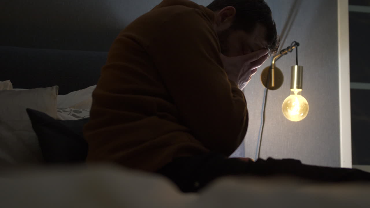 Uomo stressato con mal di testa seduto sul bordo del letto di notte