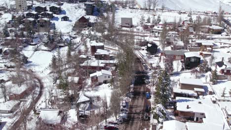 Aerial-orbit-over-the-streets-of-the-village-of-Farellones,-a-mountain-tourist-village-near-Santiago-Chile,-van-full-of-passengers-passing-through-the-snow-covered-streets,-Nordic-style-cabins