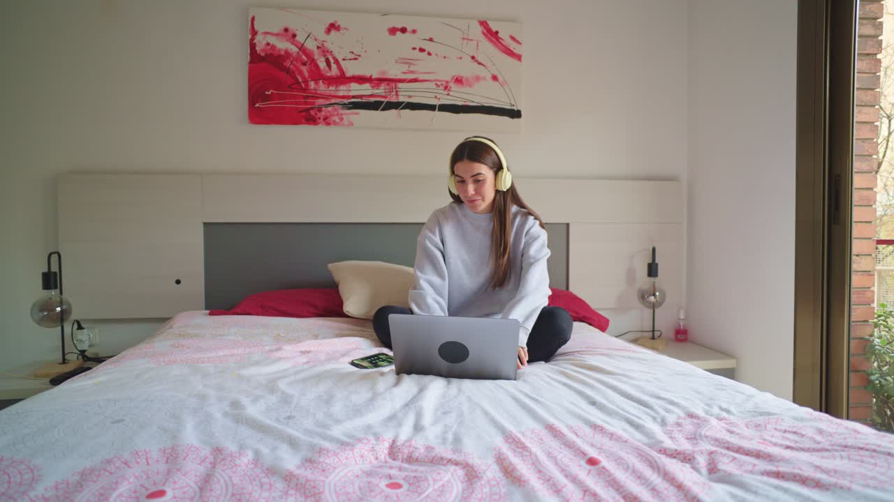 Young woman using laptop on bed with headphones