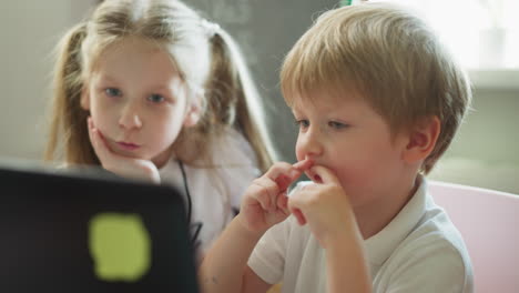 Little-siblings-watch-cartoons-on-laptop-sitting-in-room