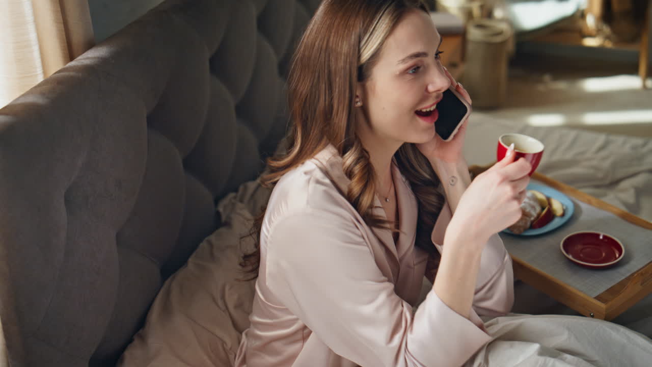 Woman talking on the phone in bed with breakfast