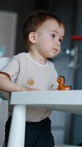beautiful child plays with a toy standing at the table. baby boy tries to climb on the chair. vertical video