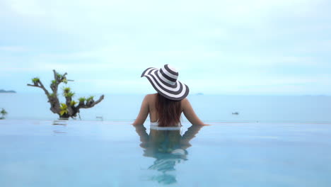 Back-of-Stylish-Female-in-Swimsuit-and-Hat-Enjoying-in-View-of-Horizon-From-Pool-Infinity