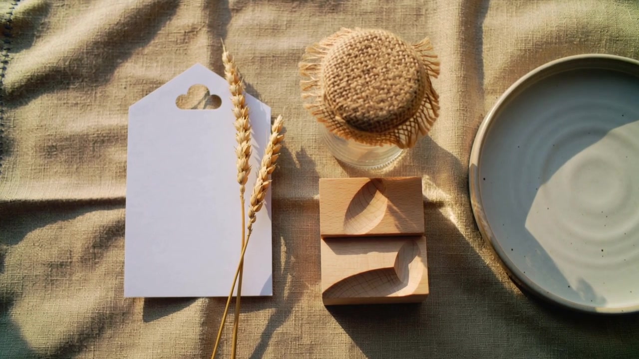 Calda luce solare che si sposta su una natura morta su lino beige, proiettando ombre su un'etichetta regalo, grano.