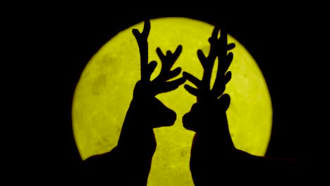 silhouette of the reindeer connecting at the yellow moon at night