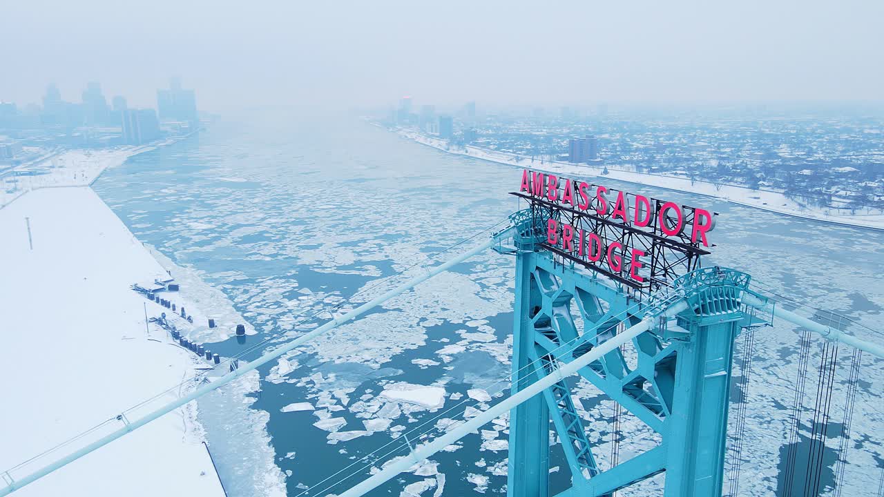 Aerial view of Ambassador Bridge tower over frozen Detroit River in winter.