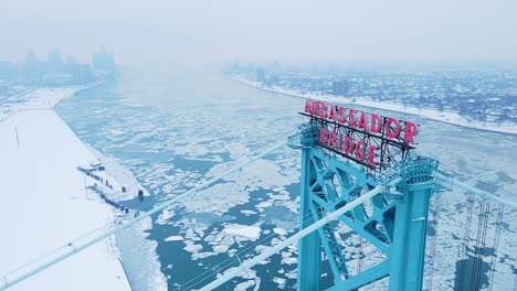 aerial view of ambassador bridge tower over frozen detroit river in winter.