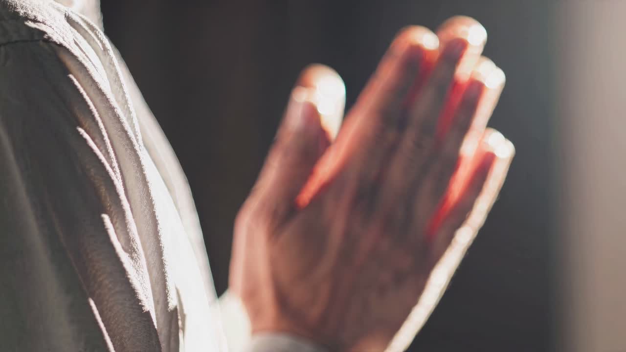 The video captures a serene moment of prayer, focusing on hands in soft lighting, conveying peace