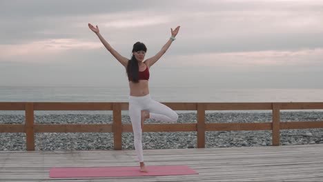 woman practicing yoga tree pose on beach