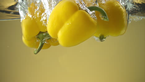 cámara lenta de pimientos amarillos cayendo al agua sobre fondo amarillo