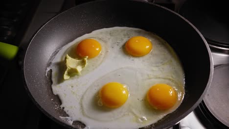 un primer plano de una sartén caliente con 4 huevos crudos, las claras se cocinan lentamente mientras un chef coloca estratégicamente trozos de aguacate en la sartén con una cuchara mientras prepara un sabroso sándwich abierto