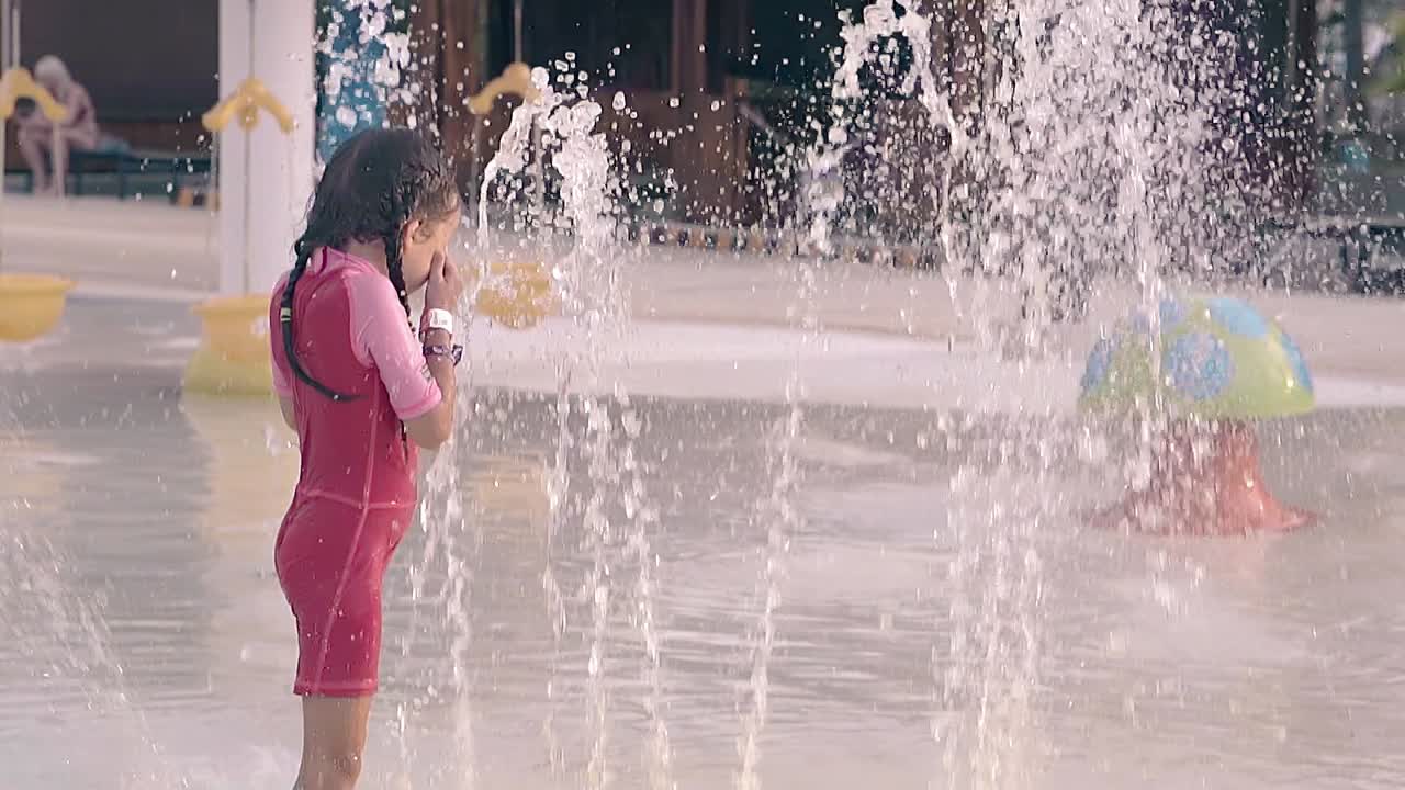 una niña bonita se encuentra entre los chorros de agua alta en cámara lenta