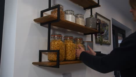 modelo femenino tomando un frasco de pasta de los estantes de la cocina en una cocina