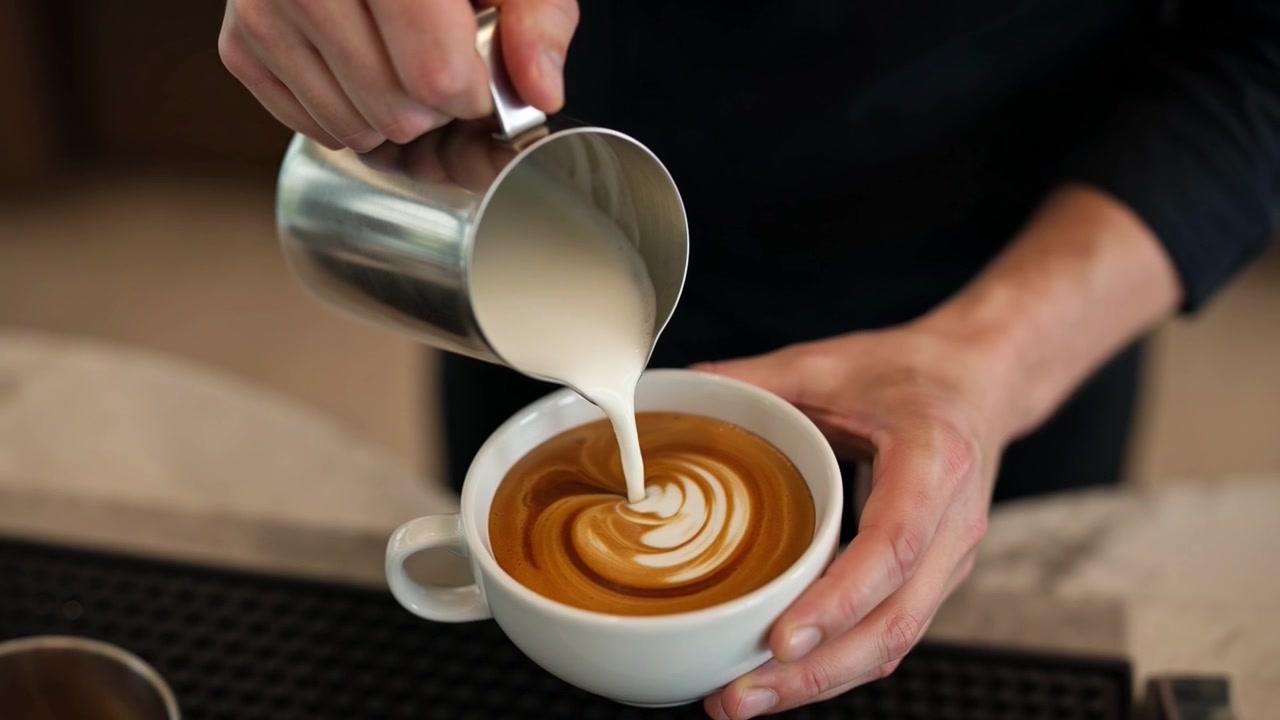 Barista che versa latte montato a vapore per creare latte art in una caffetteria