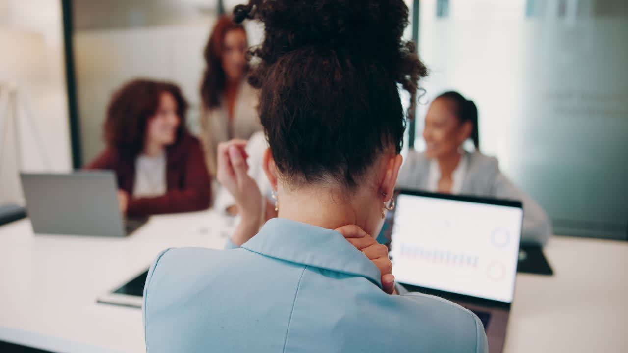 Una donna è seduta a un tavolo da conferenza con altre tre donne. Si sta massaggiando il collo, visibilmente stressata