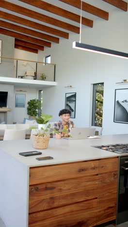 vertical video: smiling person using laptop at home in modern kitchen, enjoying coffee