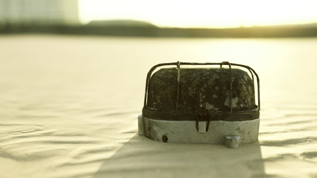 Abandoned metal object on sandy beach under warm golden sunlight