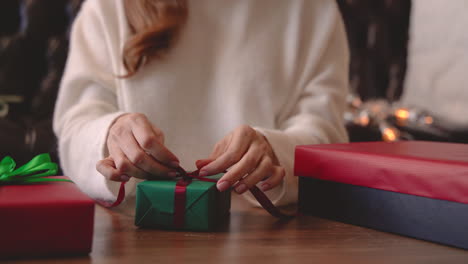 Nahaufnahme-Von-Frauenhänden,-Die-Ein-Weihnachtsgeschenk-Mit-Einer-Schleife-Auf-Einem-Tisch-Einwickeln