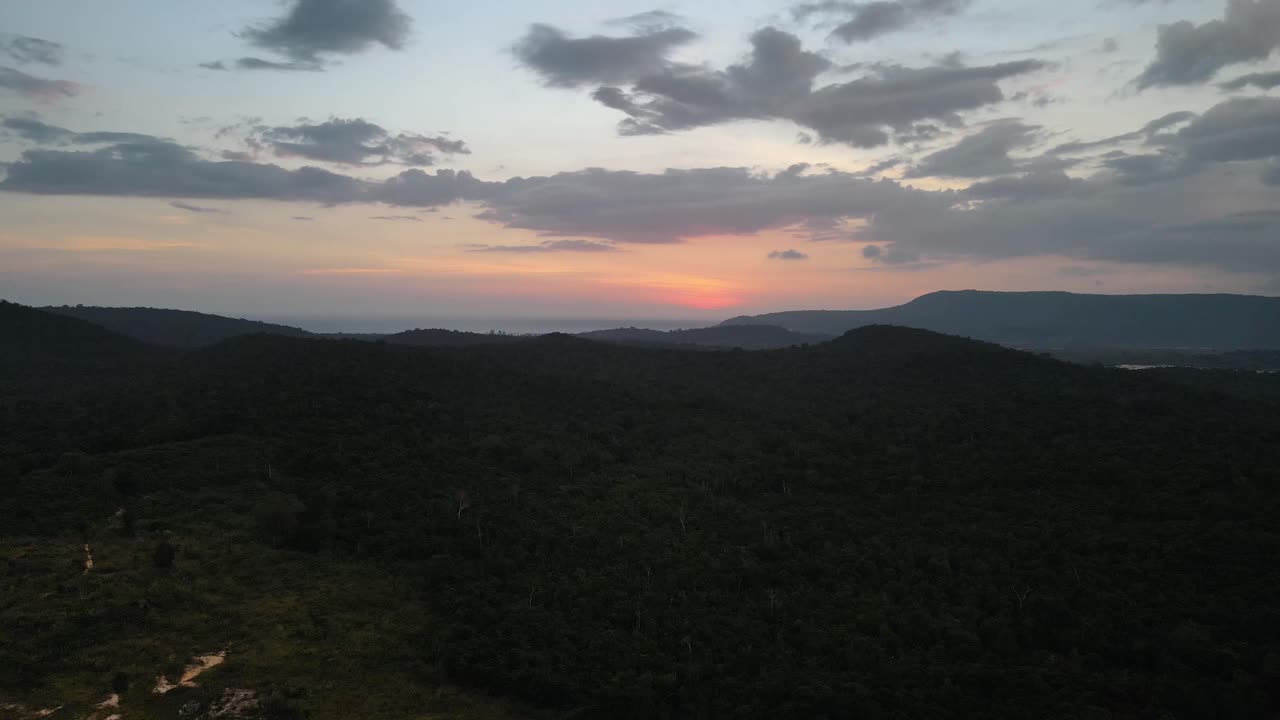 Beautiful orange colored sky through the sunset over the silhouettes of the mountains on the tourist island of Koh Rong Sanloem in Cambodia. Backwards drone dolly shot
