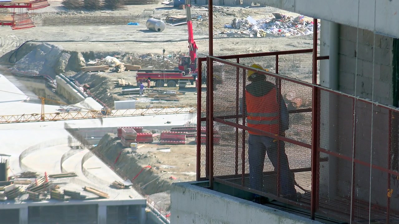 Construction Worker Standing on High-Rise Scaffolding Overlooking Site