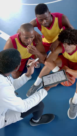 vertical video: basketball coach using tablet to explain strategy to male players on court