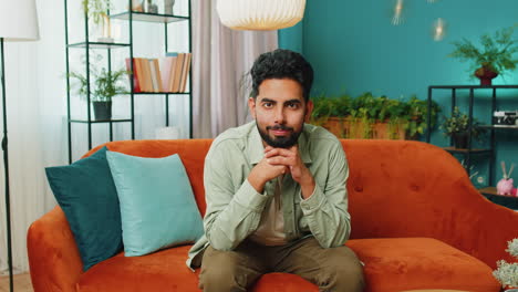 Indian-man-smiling-friendly-at-camera,-waving-hands-gesturing-hello,-hi,-greeting-at-home-on-sofa