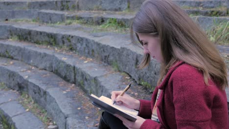 woman writing in a notebook on outdoor stone steps