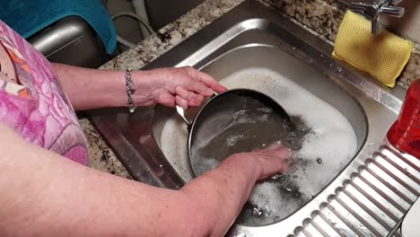 woman washing with her hands dirty steel cooking pan with detergent soap in kitchen sink