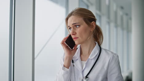 Worried practitioner talking smartphone in hospital closeup. Stressed doctor