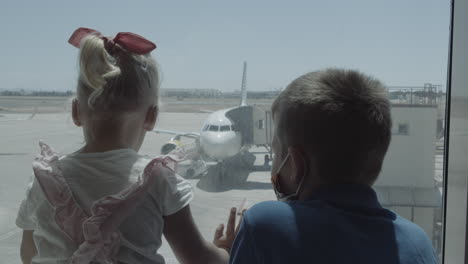 siblings are interested in planes behind the glass waiting at the airport