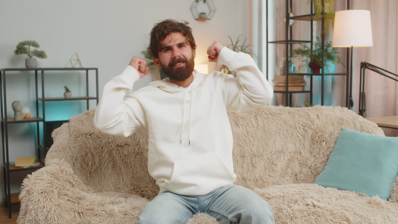 joven feliz viendo la televisión celebrando el éxito ganando la lotería suerte victoria sentado en el sofá