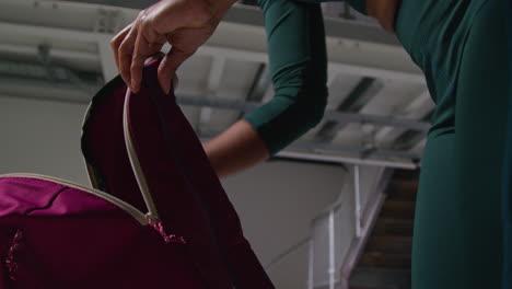 close up of woman at gym for exercise class opening zip of sports bag and taking out towel and water bottle