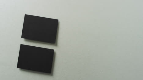 overhead view of two black business cards arranged on grey background, copy space, slow motion