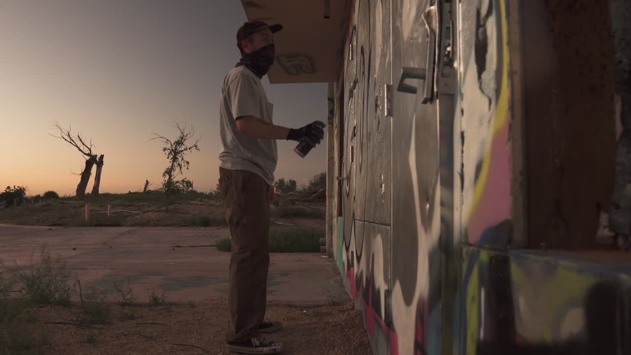 Young male street artist spray painting graffiti on abandoned building
