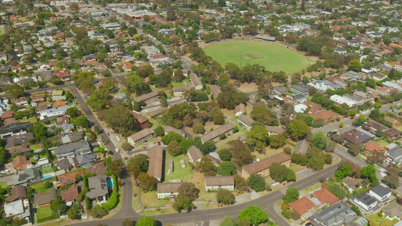 en un movimiento de cámara espiral aérea que revela las casas suburbanas y dos vastos campos de fútbol