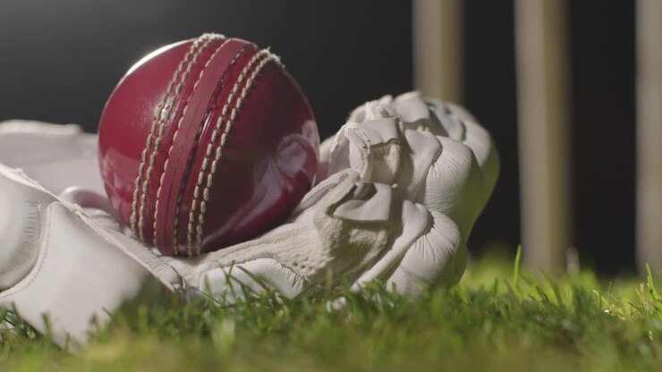 Natura morta di cricket con primo piano della palla adagiata nel guanto sull'erba davanti ai paletti 1