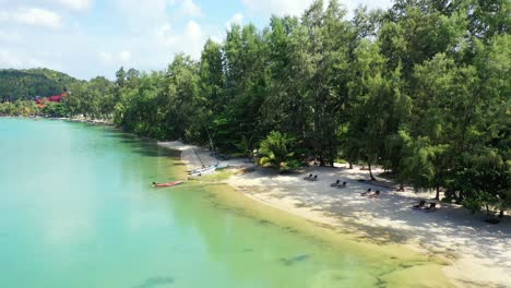 Ruhiger-Exotischer-Strand-Mit-Sonnenliegen-Im-Schatten-Wunderschöner-Tropischer-Pflanzen,-Umspült-Vom-Ruhigen-Wasser-Der-Türkisfarbenen-Lagune,-Koh-Phangan,-Thailand