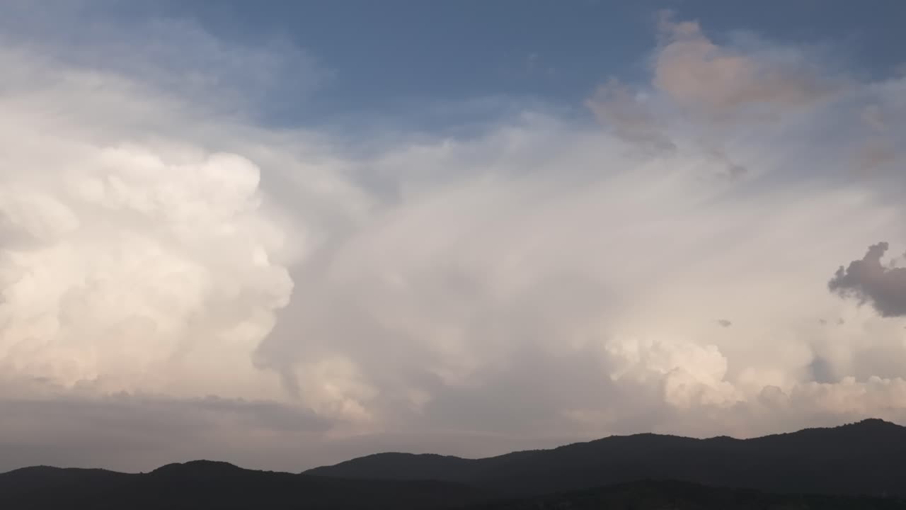 Spectacular drone filming of a large Cumulonimbus created behind a line of mountains and with a blue sky background, it is evolving and we appreciate its great width,