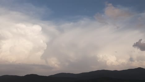 spectacular drone filming of a large cumulonimbus created behind a line of mountains and with a blue sky background, it is evolving and we appreciate its great width,