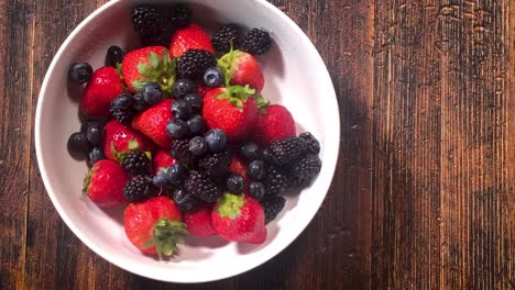 Agregando-Una-Mezcla-De-Bayas-Frescas-De-Fresas,-Arándanos-Y-Moras-Al-Bol-Sobre-La-Mesa