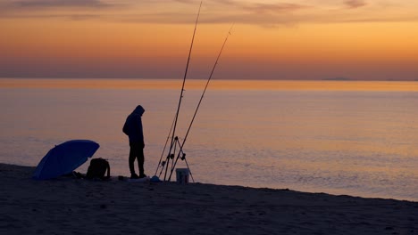 Silhouette-Einer-Person,-Die-Bei-Sonnenuntergang-Am-Meeresufer-Fischt