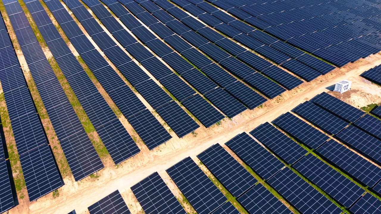 Vista dall'alto di un impianto fotovoltaico con incrocio di strade di manutenzione. Ripresa aerea con drone di file scure di pannelli fotovoltaici, sentieri sabbiosi e stazione di trasformazione in luce calda