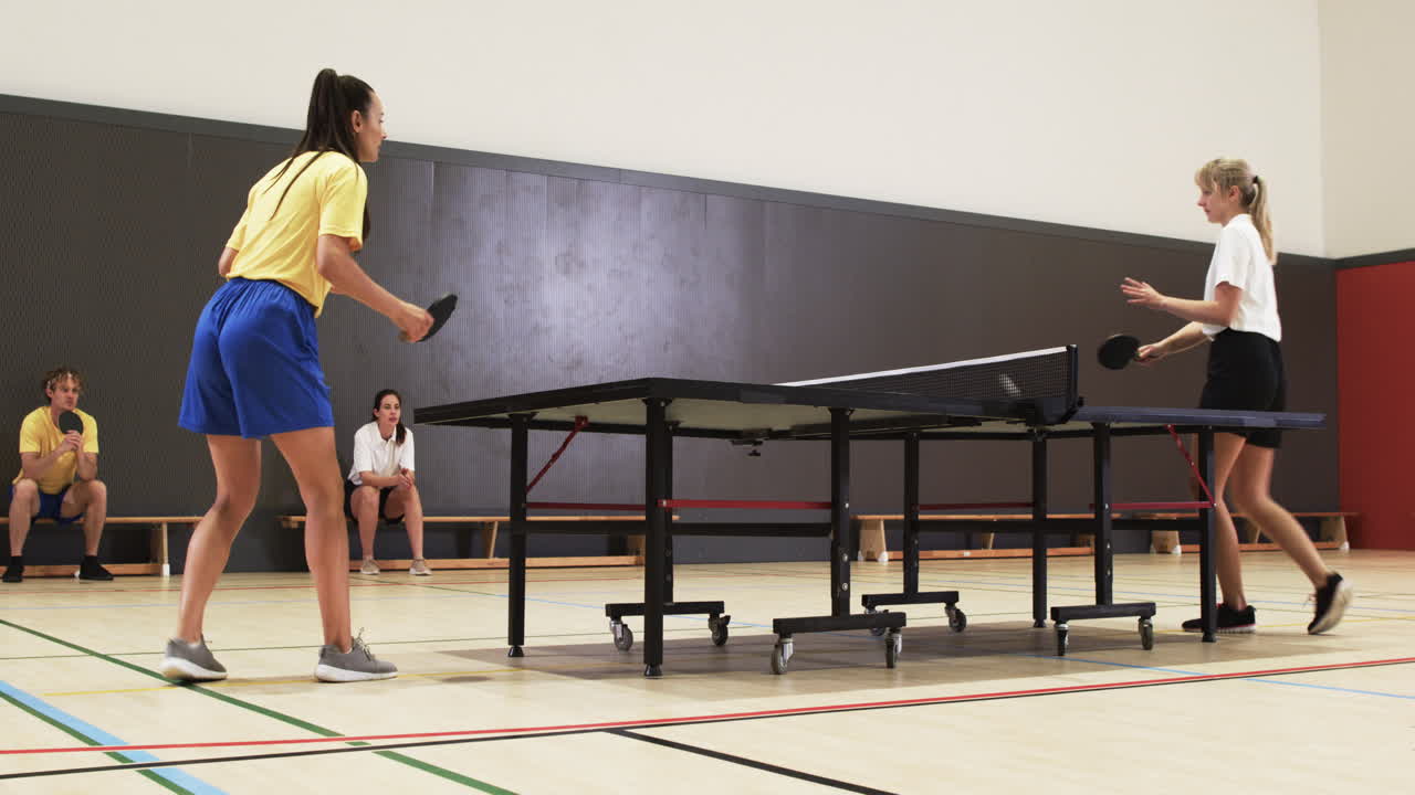 Due donne che giocano a tennis tavolo, in competizione in un impianto sportivo al coperto.