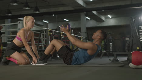 Side-view-of-caucasian-female-monitor-and-an-athletic-african-american-man-in-the-gym.