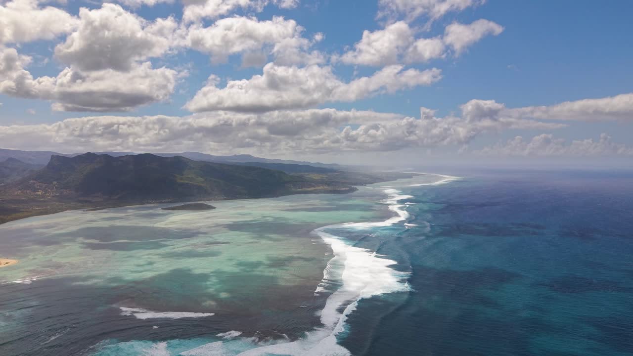 Aerial view over the coast of Mauritius, capturing the Underwater Waterfall, an optical illusion where turquoise shallows meet the deep, dark ocean near the rugged island mountains