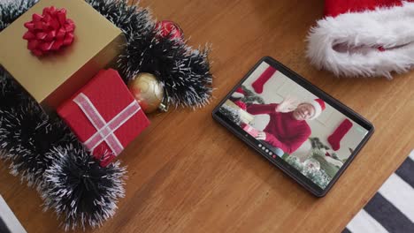 hombre albino afroamericano sonriente con sombrero de papá noel y saludando en la videollamada de navidad en la tableta