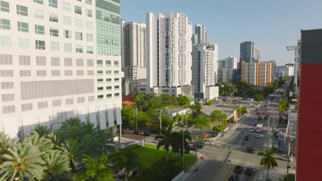 Aerial-ascending-footage-of-street-in-modern-city-in-tropical-area.-Road-lined-by-palm-trees-and-high-rise-apartment-houses.-Miami,-USA